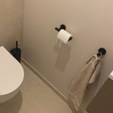 Minimalistische badkamer met een wit toilet en de Lorenzo Black WC set van yessential.nl, inclusief een zwarte toiletborstelgarnituur, handdoekhaakje en papierhouder - een strak contrast met lichte muren en vloeren.