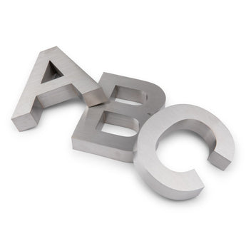 Drie grote metallic 3D letters - A, B en C - overlappen elkaar op een wit oppervlak. Hun geborstelde metalen afwerking en moderne stijl doen denken aan de Angelo RVS 20cm van yessential.nl.