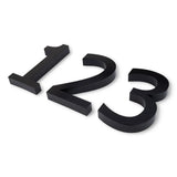 Drie grote Carlo Black huisnummers van 20 cm - 1, 2 en 3 - van yessential.nl liggen plat op een wit oppervlak en laten hun strakke moderne look zien, perfect voor elke eigentijdse ruimte.