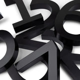 Carlo Black 20cm van yessential.nl heeft moderne, driedimensionale schreefloze cijfers in opvallend zwart, verspreid en overlappend op een wit oppervlak voor een abstracte, geometrische 3D huisnummer look.