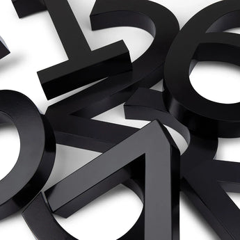 Carlo Black 20cm van yessential.nl heeft moderne, driedimensionale schreefloze cijfers in opvallend zwart, verspreid en overlappend op een wit oppervlak voor een abstracte, geometrische 3D huisnummer look.