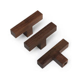 Drie Vigio Walnut Knobs van yessential.nl in donkerbruin op een witte achtergrond. De T-vormige houten knoppen zijn in verschillende hoeken geplaatst om het elegante ontwerp en de kwaliteit van het vakmanschap te laten zien.
