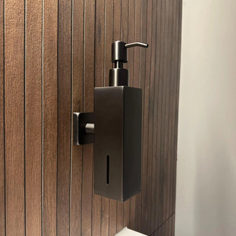 Het Sonego Gunmetal zeeppompje van yessential.nl, in strak zwart met RVS accenten, is aan de muur bevestigd op een houten lattenwand in de badkamer voor een moderne, stijlvolle look.