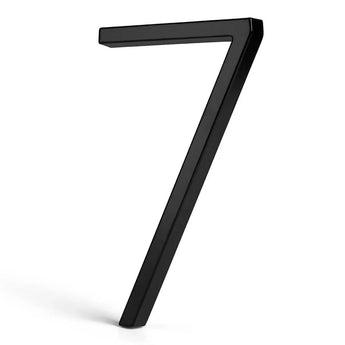 De Amato Black 15cm van yessential.nl is een driedimensionaal, zwart modern huisnummer 7 dat rechtop staat op een witte achtergrond met een vage schaduw aan de linkerkant.