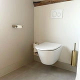 Minimalistische badkamer met een wandcloset en yessential.nl's Corrado Gold WC-set met dubbele spoeling, gouden toiletborstelhouder, wandpapierhouder en reserverol. Strak design in neutrale tinten.