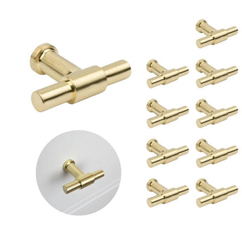 De 10x Cordero Gold Knopenset van yessential.nl heeft moderne, cilindervormige goudkleurige knoppen. Eén knop wordt apart getoond en een andere geïnstalleerd op een witte lade - ideaal voor het upgraden van je keukenkastjes.