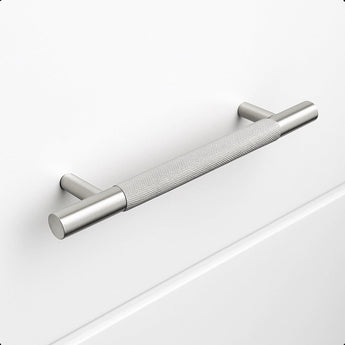De Remo RVS Deluxe van yessential.nl is een geborstelde roestvrijstalen kasttrekgreep met een greeptextuur, horizontaal gemonteerd op een effen witte lade. Hij heeft cilindrische steunen en biedt een modern, minimalistisch design.
