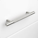 De Remo RVS Deluxe van yessential.nl is een geborstelde roestvrijstalen kasttrekgreep met een greeptextuur, horizontaal gemonteerd op een effen witte lade. Hij heeft cilindrische steunen en biedt een modern, minimalistisch design.
