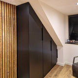 De Enzo Black kast van yessential.nl, met hoekgrepen zwart, past perfect onder een schuin plafond in een moderne kamer met houten lambrisering, lichte houten vloeren en een klein raam met jaloezieën.
