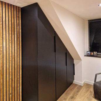 De Enzo Black kast van yessential.nl, met hoekgrepen zwart, past perfect onder een schuin plafond in een moderne kamer met houten lambrisering, lichte houten vloeren en een klein raam met jaloezieën.