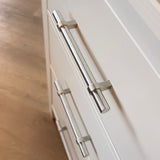 Close-up van de Arturo RVS van yessential.nl op witte kastladen, met een houten vloer op de achtergrond. De schuine foto benadrukt de bovenste handgreep-perfect voor een landelijk interieur met stijlvolle RVS handgrepen.
