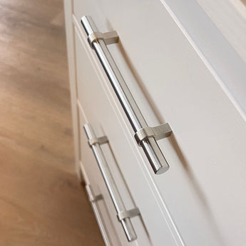 Close-up van de Arturo RVS van yessential.nl op witte kastladen, met een houten vloer op de achtergrond. De schuine foto benadrukt de bovenste handgreep-perfect voor een landelijk interieur met stijlvolle RVS handgrepen.