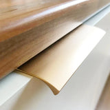 Close-up van een yessential.nl Enzo Gold Deluxe metalen profielhandgrepen kastgreep, gemonteerd onder een houten aanrechtblad en bevestigd op een wit kastoppervlak.
