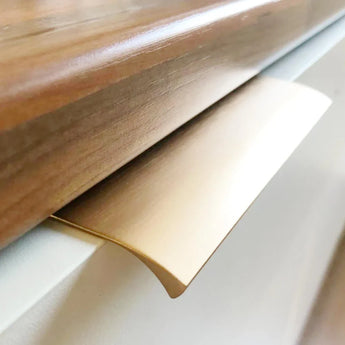 Close-up van een yessential.nl Enzo Gold Deluxe metalen profielhandgrepen kastgreep, gemonteerd onder een houten aanrechtblad en bevestigd op een wit kastoppervlak.