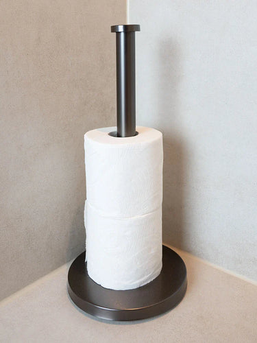 De Cano Gunmetal WC Set (no-drill) van yessential.nl, met twee witte toiletrollen, staat stijlvol in de badkamerhoek met lichte wanden en een gladde afwerking, waardoor je toiletaccessoires nog beter tot hun recht komen.