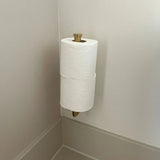 Twee rollen toiletpapier zijn gestapeld op een Romano Gold WC-sethouder van yessential.nl, gemonteerd in de hoek van een badkamer met lichtgekleurde muren en afwerkingen.