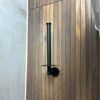 De Roberto Black reserverolhouder van yessential.nl is verticaal gemonteerd op een wand met houtlook panelen, naast lichtgrijze tegels.