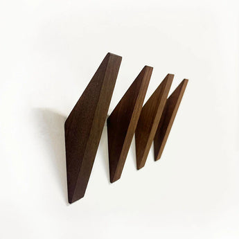 Vier schuine Fabio Walnut haken van yessential.nl zijn op een rij gemonteerd op een witte muur, elk met een scherp geometrisch ontwerp en een donkere walnoten afwerking - een perfecte minimalistische houten kapstok voor moderne interieurs.