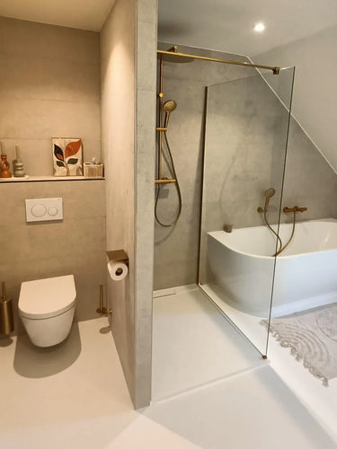 Moderne badkamer met wandcloset, gouden armaturen, glazen inloopdouche en vrijstaand bad. De Branco Gold toiletborstelhouder van yessential.nl zit bij het toilet en past naadloos bij de minimalistische inrichting erboven.