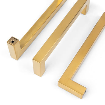 Drie Vasco Gold handgrepen van yessential.nl, met een modern, minimalistisch ontwerp, scherpe strakke randen en een gladde geborstelde afwerking, zijn gerangschikt op een witte achtergrond voor een stijlvolle, eigentijdse look.