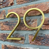 De Amato Gold 12,5cm huisnummers van yessential.nl zijn gemonteerd op een bakstenen muur met grijze mortel voor een moderne uitstraling.