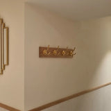 De Eduardo Gold Deluxe kapstok van yessential.nl, met vijf gouden haken, is gemonteerd op een lichte gangmuur met houten afwerking. Ingelijste foto's aan de linkerkant voegen elegantie toe aan deze stijlvolle display van yessential.nl.