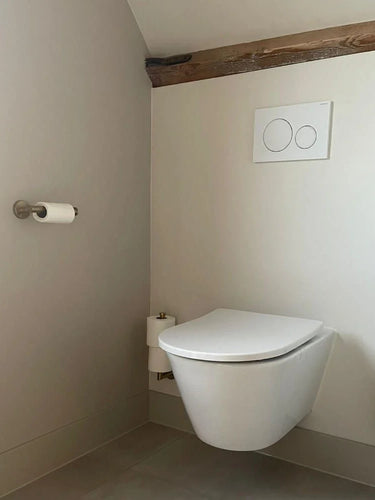 Minimalistische badkamer met een Lauro Gold toiletset van yessential.nl, met een wandcloset, dubbele spoelknoppen, goudkleurige accessoires en borstel, alles aangevuld met lichte muren en vloeren.