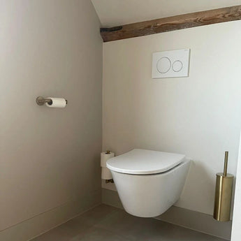 Een minimalistische badkamer met de yessential.nl Xavo Gold WC set met een wandcloset, dual-flush knoppen en bijpassende gouden toiletaccessoires op lichtgekleurde muren en vloer.