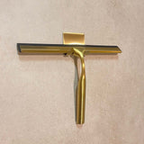De Zamoro Gold van yessential.nl, met een gouden handvat en zwart blad, is verticaal gemonteerd op een muur met beige structuur en een 3M ophangsysteem.