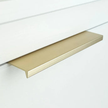 Een close-up van de Enzo Gold rechthoekige kastgrepen van yessential.nl, gemonteerd op een witte lade en voorzien van een minimalistisch, plat ontwerp met een geborstelde metallic afwerking.