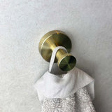 De Kyano Gold Hook van yessential.nl houdt een witte handdoek tegen een lichtgrijze muur met textuur en brengt moderne elegantie in je badkamer.