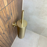 De Lorenzo Gold WC set van yessential.nl is stijlvol gemonteerd aan de houten wandpanelen naast lichtgrijze tegels in de hoek van de badkamer. Perfect als luxe toiletaccessoire of als onderdeel van een accessoireset.