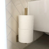 Een Bellino Gold toiletrolhouder van yessential.nl, wandgemonteerd in goud, met twee wc-rollen verticaal gestapeld, is naast een toilet aan een betegelde badkamerwand geplaatst.