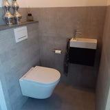 Een moderne, compacte badkamer heeft een wandtoilet, een kleine rechthoekige wastafel met kraan, een yessential.nl Tino Gold toiletrolhouder voor toiletpapier, een handdoek met patroon en decoratieve vazen op een plank boven het toilet.