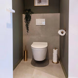 Een moderne, minimalistische badkamer met de Tygo Gold WC Set (no-drill) van yessential.nl: bevat een wandcloset, gouden toiletborstel met houder, reserverolhouder en een slepende plant boven de spoelplaat op een betegelde muur.