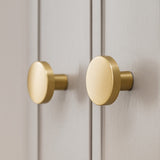 Twee ronde Marizo Gold knoppen van yessential.nl zijn geïnstalleerd op lichtgrijze kastdeurtjes, te zien in close-up. Deze elegante knoppen hebben een geborstelde gouden afwerking die glad en licht reflecterend is.