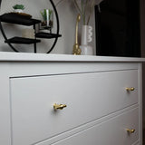 Een wit dressoir met de Rando Gold Knob van yessential.nl in een rond design staat voor een plank met kleine plantjes en decor. Vazen en een gouden vogelfiguurtje bovenop maken het ideaal voor een moderne interieurstijl.