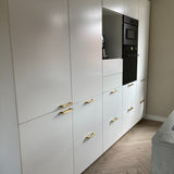 Moderne keuken met witte kasten, Vasco Gold handgrepen van yessential.nl, ingebouwde zwarte oven en lichthouten visgraatvloer. Neutrale muren en een minimale inrichting zorgen voor een strakke, strakke look.
