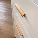 Close-up van twee Lucasso Eiken handgrepen op crèmekleurige lades, met houten vloer op de achtergrond.