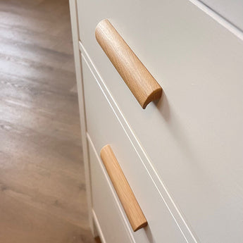 Close-up van twee Lucasso Eiken handgrepen op crèmekleurige lades, met houten vloer op de achtergrond.