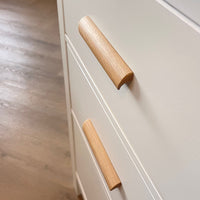 Nahaufnahme von zwei Griffen aus Lucasso-Eiche an cremefarbenen Schubladen, mit Holzboden im Hintergrund.