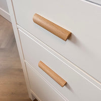 Close-up van eikenhouten handgrepen in een moderne minimalistische stijl. De lades maken deel uit van een kast op een lichthouten vloer.