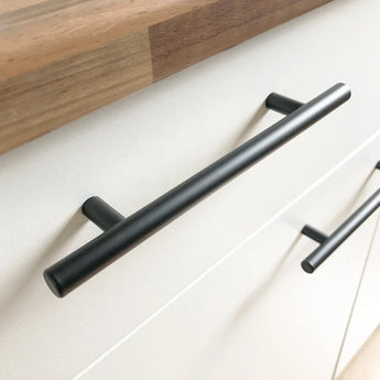 Remo zwarte kastgrepen van yessential.nl hebben een cilindrisch, horizontaal ontwerp. Deze zwarte handgrepen, geïnstalleerd op witte lades met een houten aanrechtblad, geven elke keuken een moderne, minimalistische uitstraling.