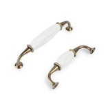 De Daro Ceramic Antique Gold kastgrepen van yessential.nl hebben gebogen antiekgouden uiteinden en een wit keramisch midden, weergegeven op een witte achtergrond - perfect om tijdloze charme toe te voegen aan elke kast.