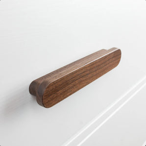 Een close-up van de Arriero Walnut houten handgrepen van yessential.nl, met zijn gladde, ovale vorm, natuurlijke houtnerfafwerking en afgeronde hoeken bevestigd aan een wit ladefront.