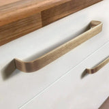 Close-up van twee Leonardo Gold Deluxe meubelgrepen van yessential.nl in goudkleurig op witte lades onder een houten aanrechtblad. De grotere luxe handgreep zit op de bovenste lade, de kleinere op de onderste lade.