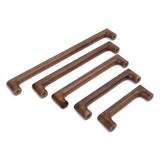 Vijf Salgado Walnut handgrepen van yessential.nl, elk met een strak, modern ontwerp en afgeronde hoeken, zijn diagonaal geplaatst op een wit oppervlak. Zichtbare schroefgaten accentueren de verschillende lengtes van deze houten handgrepen.