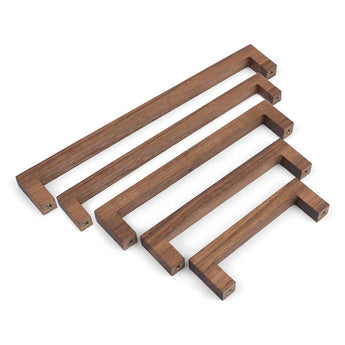 Vier Vasco Walnut handgrepen van yessential.nl in walnotenhout, diagonaal gerangschikt van groot naar klein op een witte achtergrond. Elk handvat heeft zichtbare schroefgaten aan beide uiteinden.