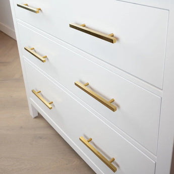 Het Marano Gold dressoir van yessential.nl heeft drie lades met horizontale gouden moderne meubelgrepen, geplaatst op een lichte houten vloer voor een strakke, moderne uitstraling.
