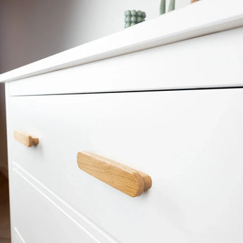 Close-up van het Arriero Oak dressoir van yessential.nl, met grote, minimalistische eikenhouten handgrepen. Dit moderne witte dressoir toont enkele decoratieve items op het bovenblad.